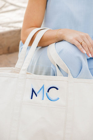 A canvas tote is embroidered with blue initials. 