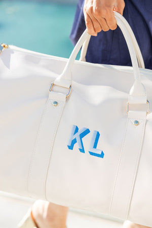 A person holds a white duffel with a bold blue monogram embroidered on it.
