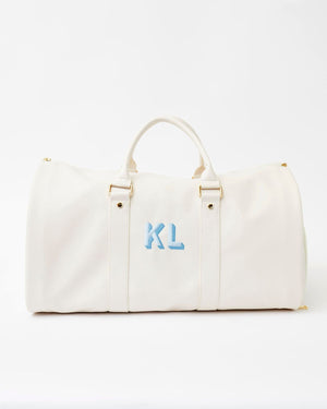 A white duffel bag is personalized with a blue monogram.