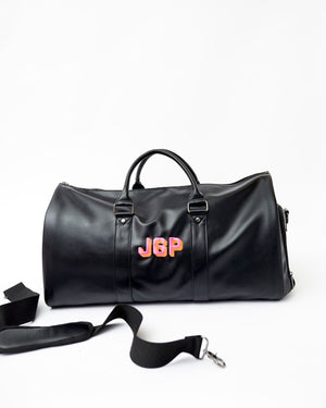 A black duffel bag is monogrammed with a pink and orange thread.