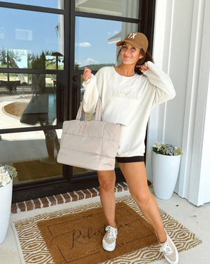 A brunette wears a monogrammed corduroy baseball hat, a personalized puffer tote, and a custom corded sweatshirt