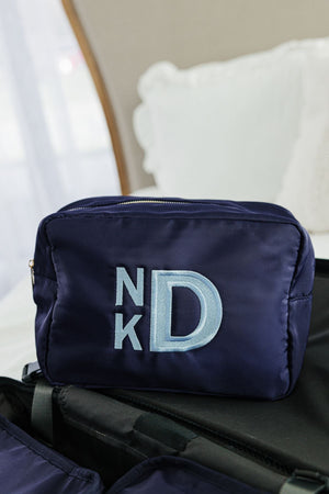 A navy nylon pouch is customized with a light blue embroidered monogram.