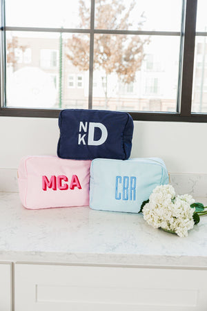 A few custom monogram nylon pouches are stacked next to some flowers