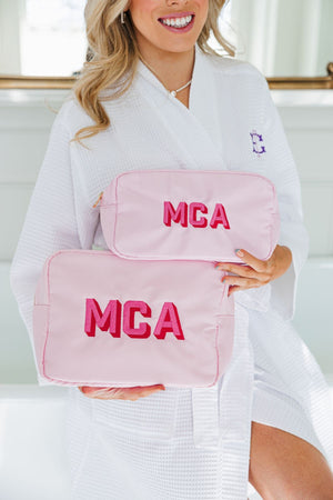 A woman holds up a large and an extra large nylon pouch with pink embroidery.