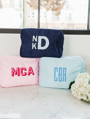 A few custom monogram nylon pouches are stacked next to some flowers