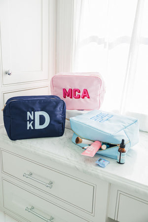 A group of nylon pouches are embroidered with monograms and filled with bathroom products.
