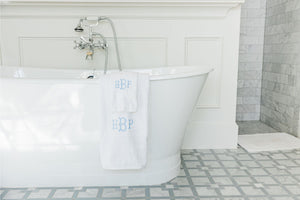 A bath towel and hand towel are customized with matching monograms and draped over the side of a bathtub.