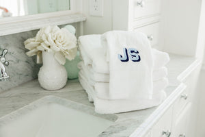 A stack of monogrammed towels are folded up next to a bathroom sink