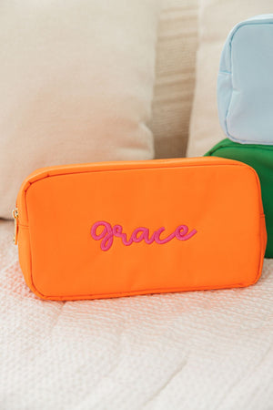 An orange nylon pouch with "Grace" embroidered in pink