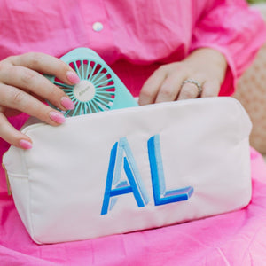 A woman puts a mini fan in her white, monogrammed pouch