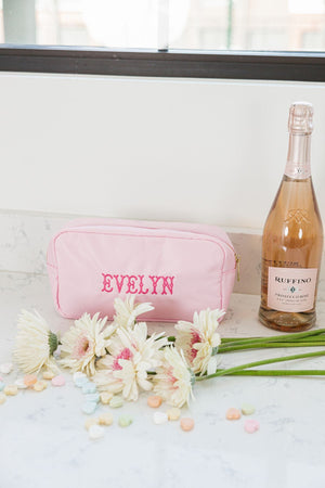 A pink nylon pouch is embroidered with the name "Evelyn" in bright pink thread.