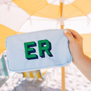A woman holds a blue pouch with "ER" monogrammed in green 
