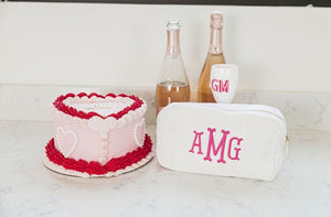 A white nylon pouch is customized with a pink monogram and placed with a cake and wine.