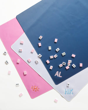 Three monogrammed Mahjong tile mats in white, blue, and pink have tiles laying on them
