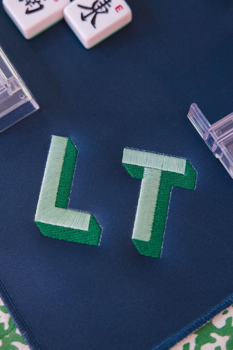 A green, embroidered monogram on a dark blue mahjong tile mat
