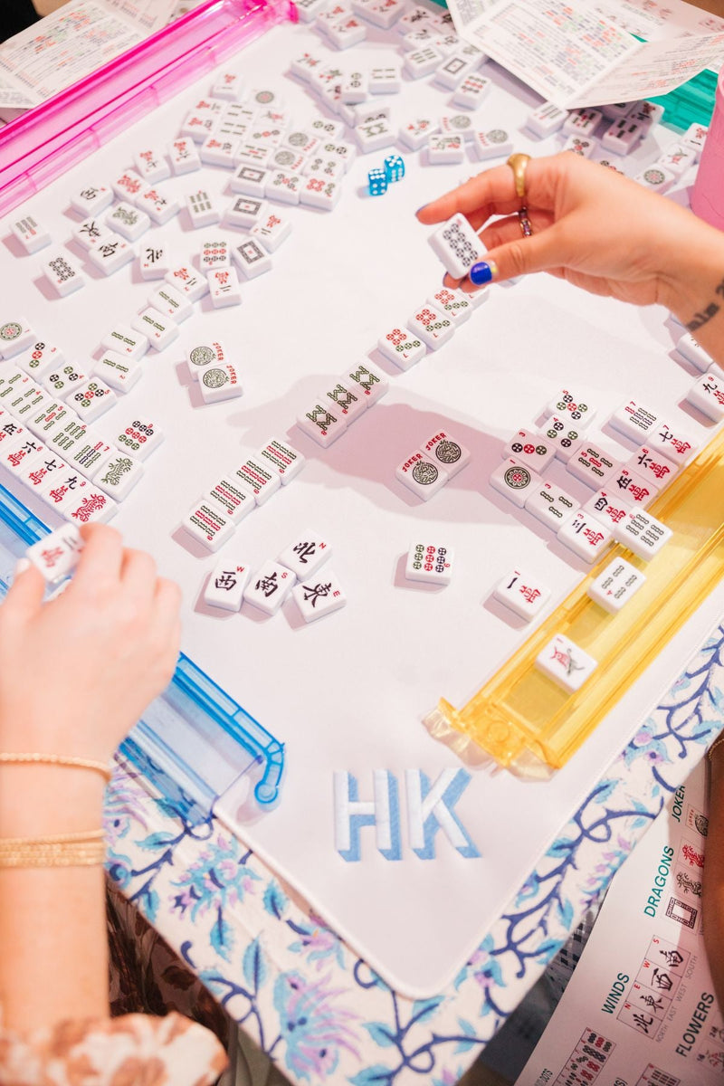 A person playing mahjong on a white mat with an embroidered monogram on it