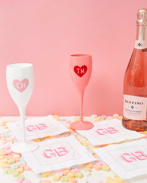 A set of monogrammed cocktail napkins is set up with a bottle of champagne and some champagne flutes