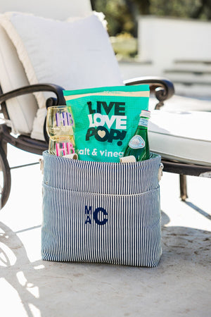  A navy cooler bag is monogrammed and filled with aa bag of popcorn, a water botte, and some monogrammed wine glasses.