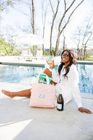 A girl sits in front of a pool next to her customized cooler bag and drinks a glass of wine.