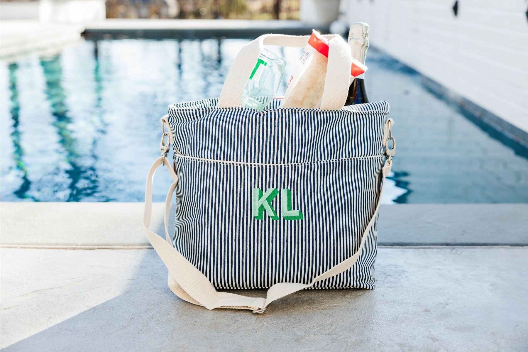 A monogrammed pink and navy stripped cooler tote are filled with snacks and drinks.