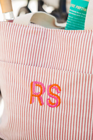 A pink and orange monogram is embroidered onto a pink striped cooler tote