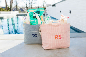 A navy and a pink cooler tote are monogrammed and filled with snacks and monogrammed cups.