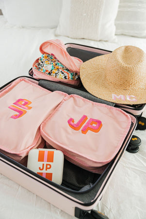A suitcase is packed full of personalized products including a white jewelry case, a set of pink packing cubes and a straw beach hat.