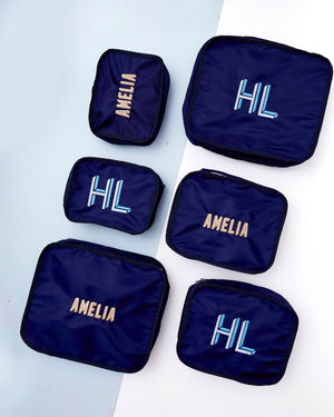 An array of navy packing cubes are embroidered with custom names and monograms.