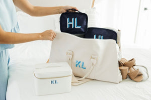 A set of navy packing cubes with a monogram is placed into a white duffel.