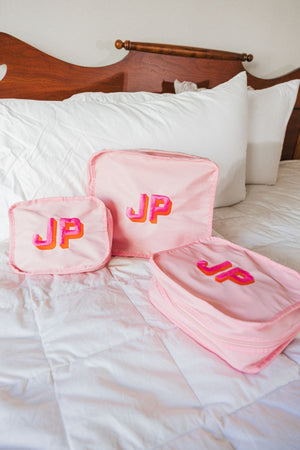 A set of pink packing cubes is embroidered with a pink and orange monogram.