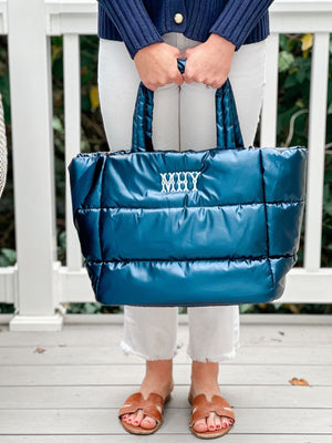 A woman holds a blue puffer tote with her monogram embroidered on the front