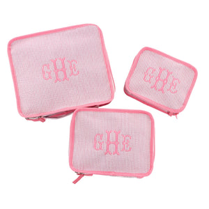 Three pink seersucker packing cubes lay flat showing off their pink embroidered monograms.