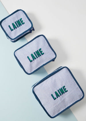 A set of three navy packing cubes is set up to show off their different sizes and embroidered customization.
