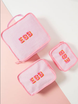 A set of three pink packing cubes is set up to show off their different sizes and embroidered customization.