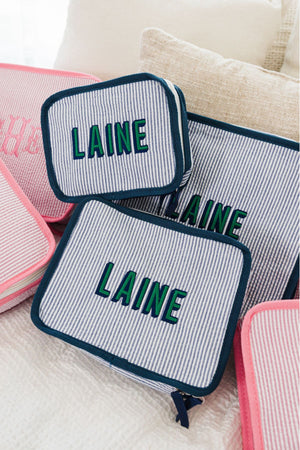 A set of navy packing cubes is customized with a last name in green and navy block font. 