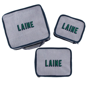 A set of three navy packing cubes is set up to show off their different sizes and embroidered customization.