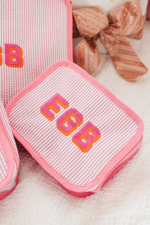 A pink seersucker packing cube is seen up close to show off it's customized monogram in pink and orange.