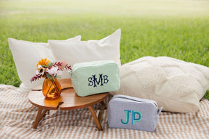 Two monogrammed seersucker bags one blue and one green sit on a picnic blanket