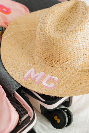 A straw hat is customized with a pink monogram.