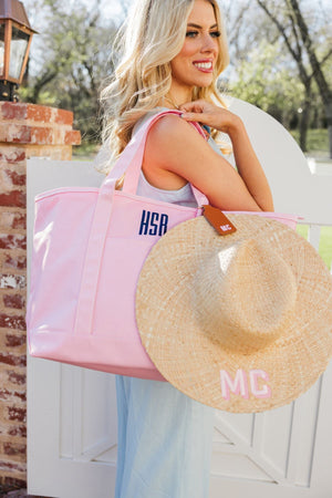 A girl holds a monogrammed pink tote with a hat attached with a tan hat clip with a pink monogram.