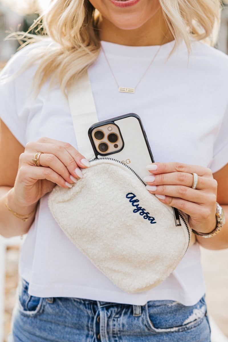 A woman in a white shirt puts her phone into her personalized belt bag with her name on it.