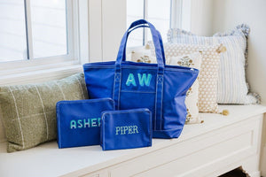 A matching blue tote bag and two roadie pouches are personalized with similar mint monograms and names.