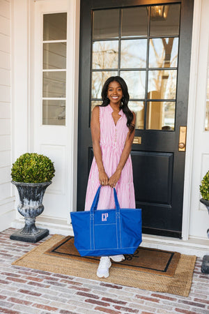 A woman in a pink striped dress holds a blue tote bag with a pink monogram.