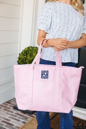 A woman holds a pink tote bag with a navy monogram embroidered on it.