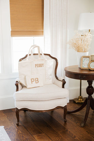 A cream tote bag and a cream roadie are personalized with beige and tan embroidered personalization.