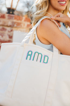 A woman holds a cream tote bag with a colorful monogram.