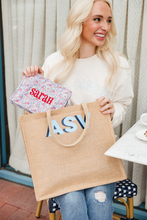 A blonde puts her embroidered travel roadie into a monogrammed jute tote bag