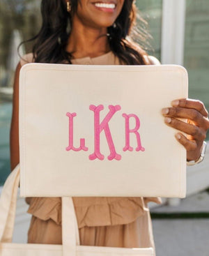 A woman holds up a cream roadie with a pink monogram on it.