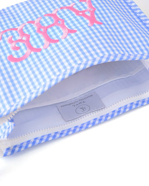 A blue pouch with a pink monogram lays open showing the pockets on the inside.