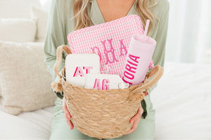 A person in green pajamas holds up a basket of pink and white customized gifts.